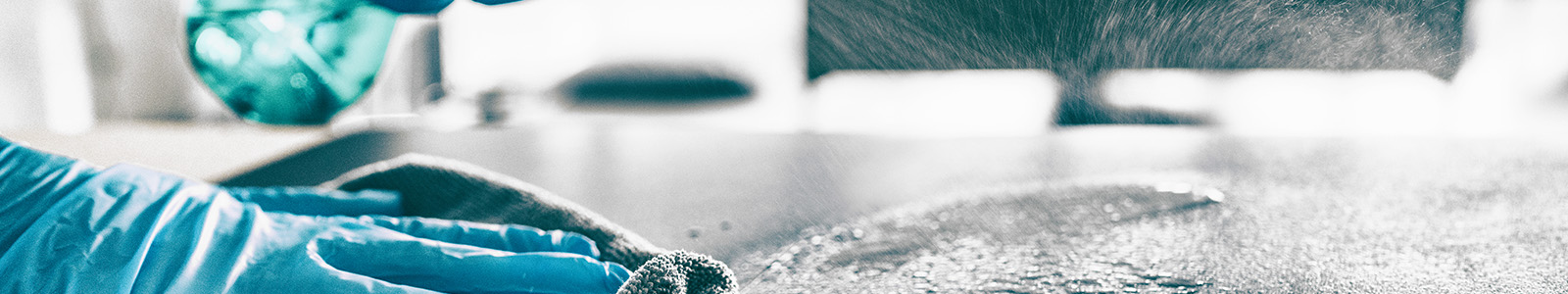 Bottle of cleaning spray being used to disinfect a surface by a gloved hand