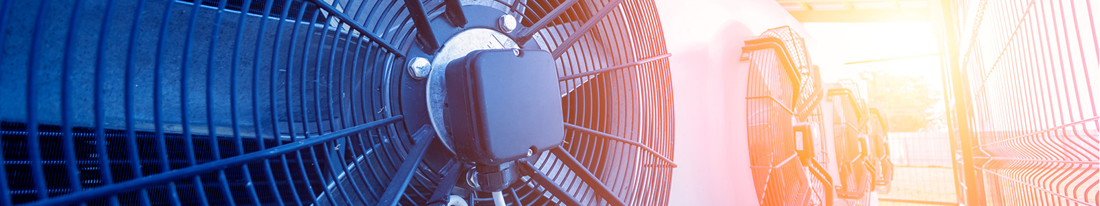 Multiple HVAC fan units on a commercial building rooftop with a sunset in the background