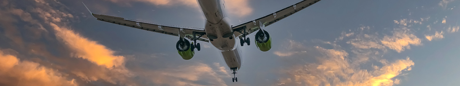 Under shot of airplane flying with sunset in the background