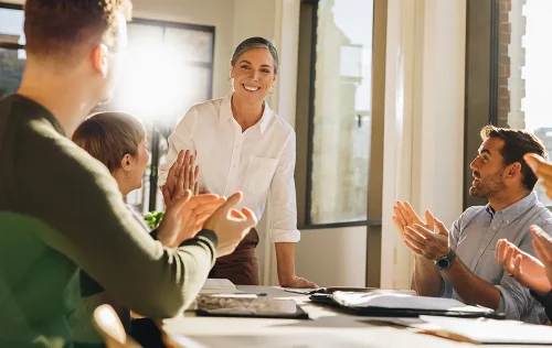 Professional woman smiling as colleagues celebrate and applause in conference room